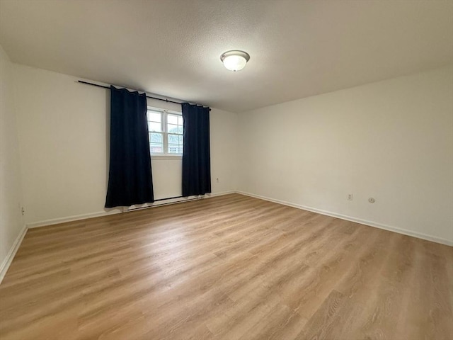 spare room with light wood-type flooring, baseboards, and a textured ceiling