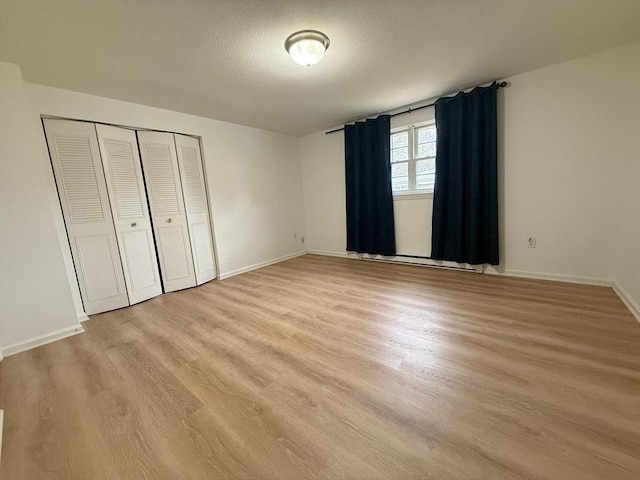 unfurnished bedroom featuring a closet, baseboards, light wood finished floors, and a textured ceiling