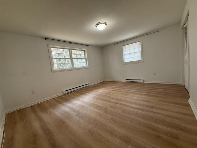 spare room featuring light wood-style flooring, a baseboard heating unit, and baseboards