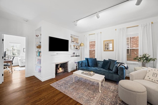 living room featuring rail lighting, dark wood-style flooring, plenty of natural light, and built in shelves