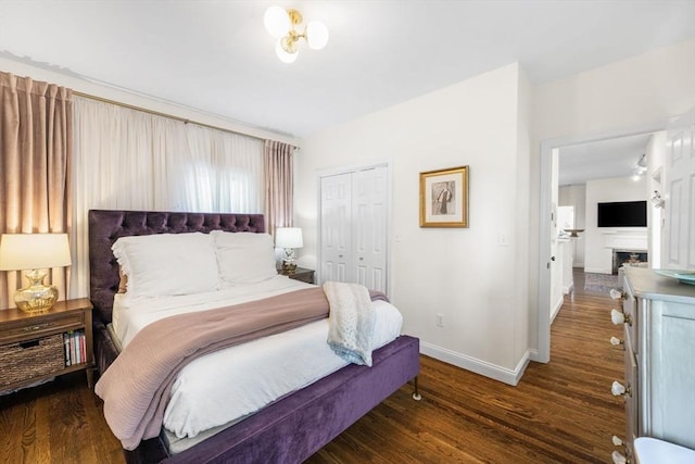 bedroom with wood finished floors, baseboards, a closet, and a fireplace