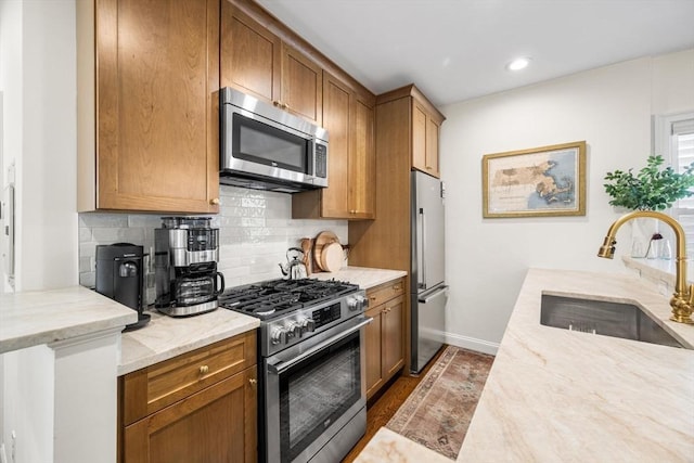 kitchen featuring stainless steel appliances, a sink, backsplash, light stone counters, and baseboards