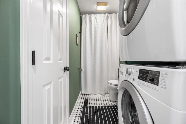 laundry room featuring stacked washing machine and dryer, tile patterned flooring, and baseboards
