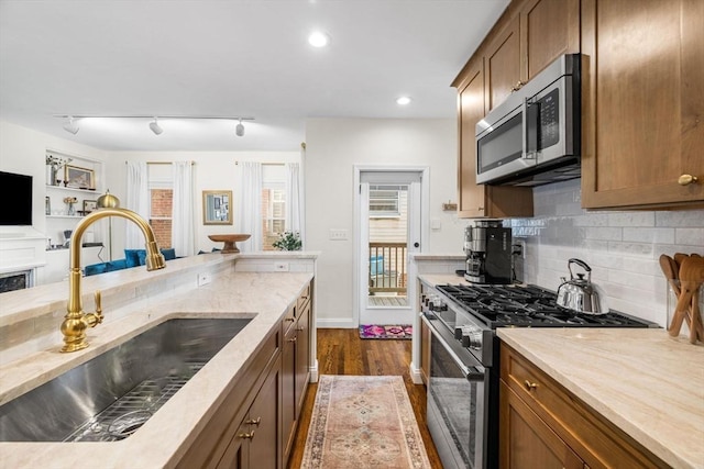kitchen with appliances with stainless steel finishes, a sink, decorative backsplash, light stone counters, and track lighting