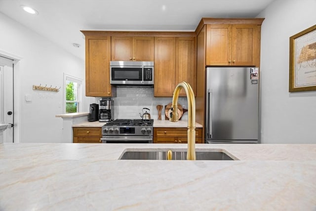 kitchen featuring appliances with stainless steel finishes, a sink, brown cabinets, tasteful backsplash, and recessed lighting