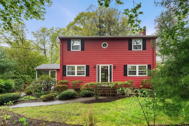 colonial house featuring a chimney and a front yard