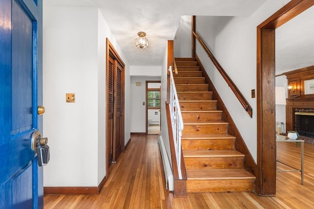 entrance foyer with stairway, wood finished floors, a baseboard radiator, and baseboards