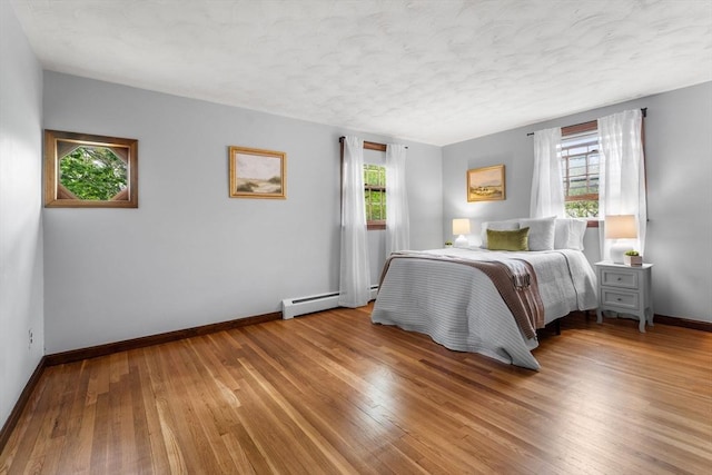 bedroom with baseboards, wood finished floors, a textured ceiling, and a baseboard radiator