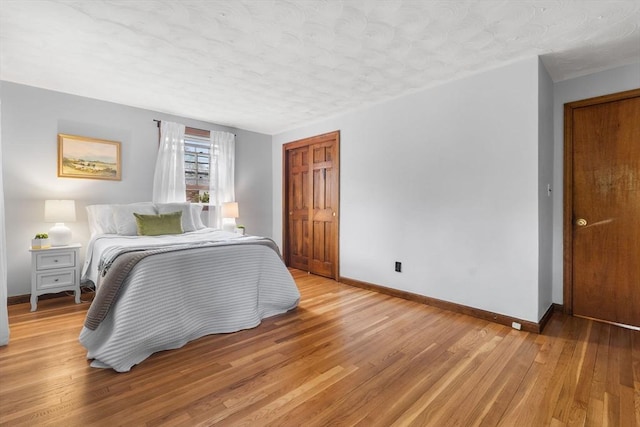 bedroom featuring a textured ceiling, light wood-style flooring, baseboards, and a closet