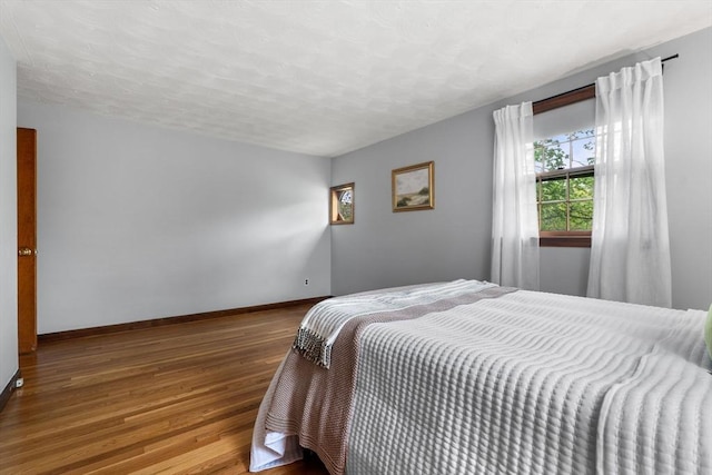 bedroom featuring wood-type flooring, baseboards, and a textured ceiling
