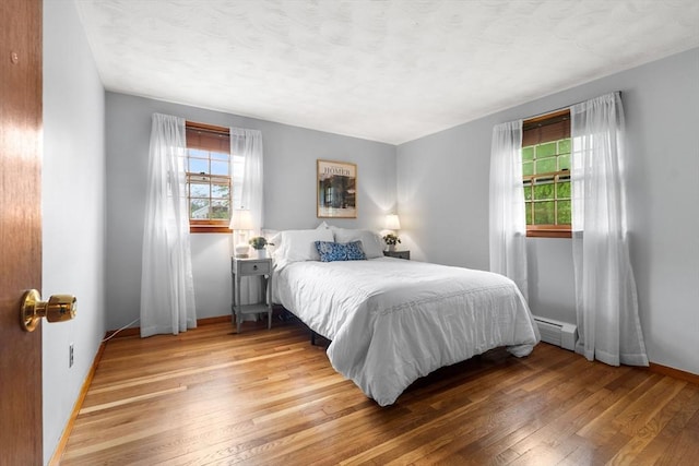 bedroom featuring multiple windows, baseboards, and light wood finished floors