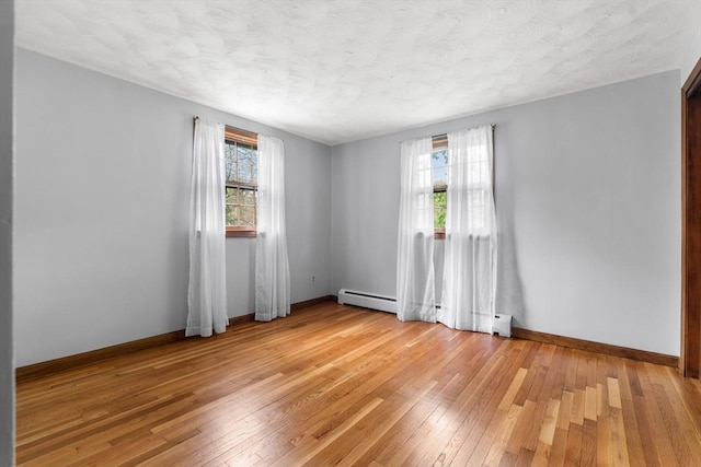 spare room featuring plenty of natural light, light wood-style floors, baseboards, baseboard heating, and a textured ceiling