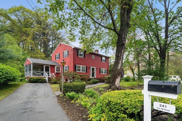 view of front of home featuring a sunroom, a chimney, and asphalt driveway
