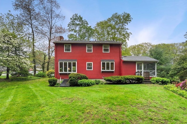 rear view of house with a sunroom, a chimney, and a lawn