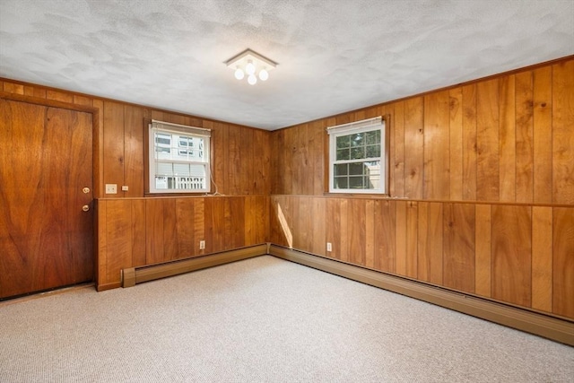 carpeted empty room with a textured ceiling, baseboard heating, and wooden walls