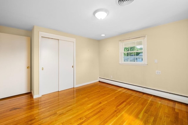 unfurnished bedroom with baseboards, visible vents, a baseboard radiator, a closet, and light wood-type flooring