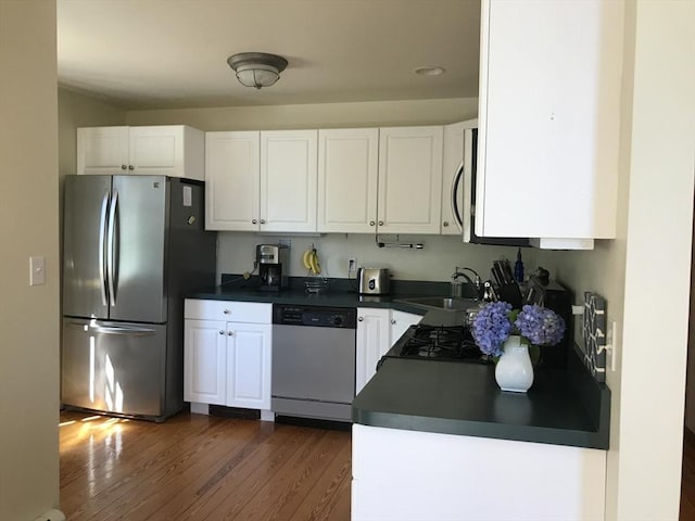 kitchen featuring stainless steel appliances, dark countertops, a sink, and white cabinetry