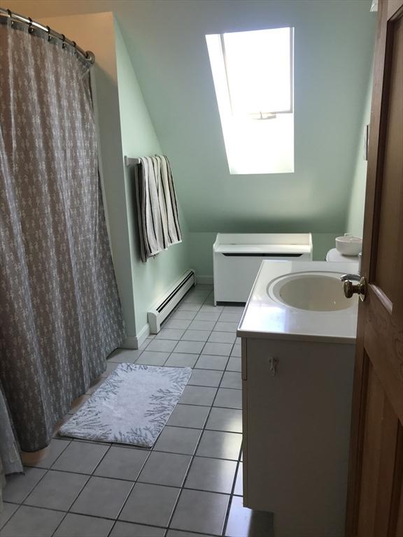 bathroom with lofted ceiling with skylight, a baseboard radiator, a shower with curtain, tile patterned flooring, and vanity