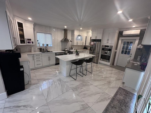 kitchen with appliances with stainless steel finishes, wall chimney exhaust hood, sink, white cabinets, and a center island