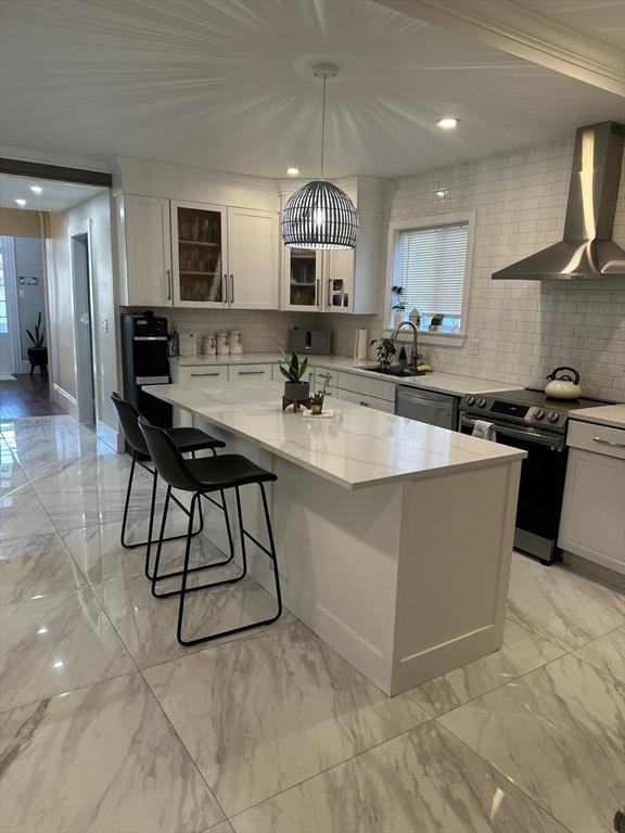 kitchen featuring white cabinets, appliances with stainless steel finishes, a center island, and wall chimney exhaust hood