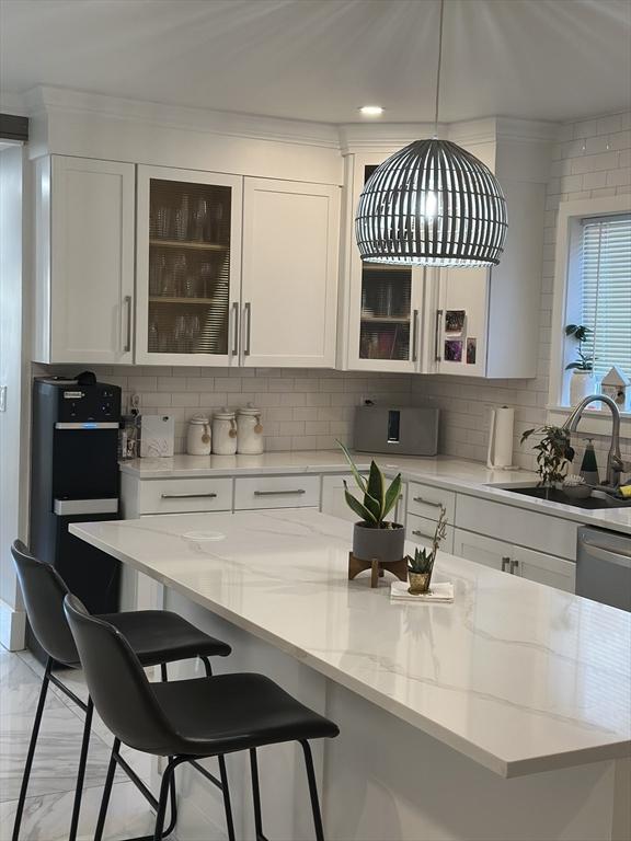 kitchen featuring white cabinetry, light stone countertops, sink, hanging light fixtures, and decorative backsplash