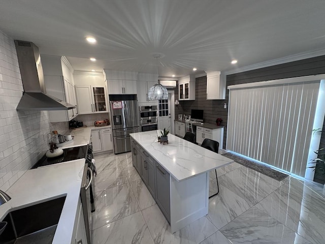 kitchen featuring a center island, wall chimney exhaust hood, stainless steel appliances, tasteful backsplash, and decorative light fixtures