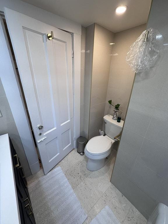 bathroom with toilet and tile walls