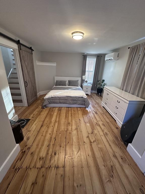 unfurnished bedroom with a wall mounted AC and light hardwood / wood-style flooring