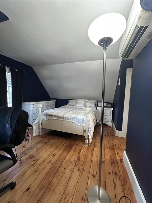 bedroom featuring an AC wall unit, light hardwood / wood-style floors, and vaulted ceiling