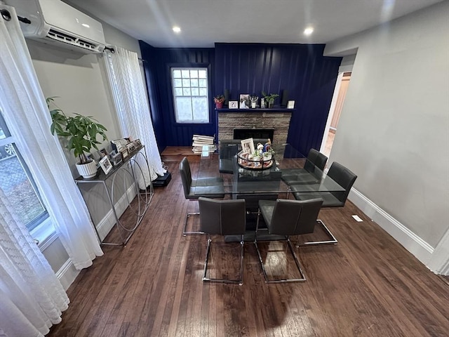 dining room with dark hardwood / wood-style floors, an AC wall unit, and a stone fireplace