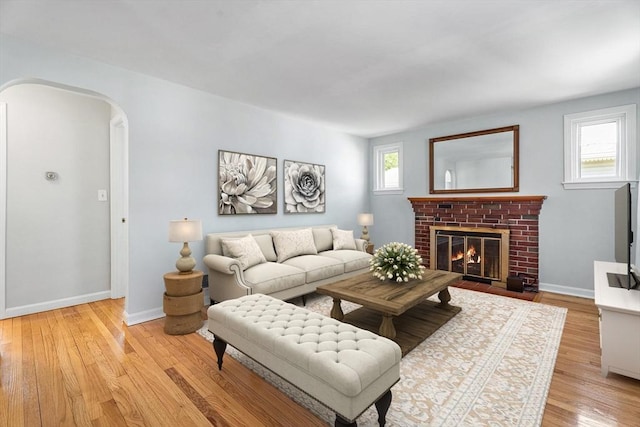 living room with light wood-type flooring, arched walkways, baseboards, and a fireplace
