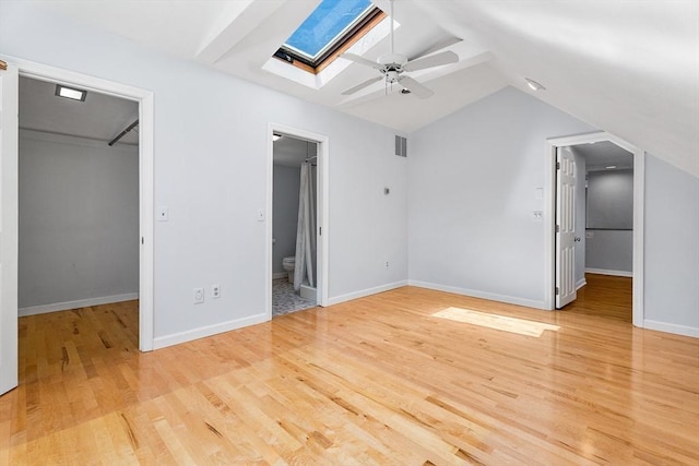 unfurnished bedroom with visible vents, a closet, lofted ceiling with skylight, a spacious closet, and light wood-style floors