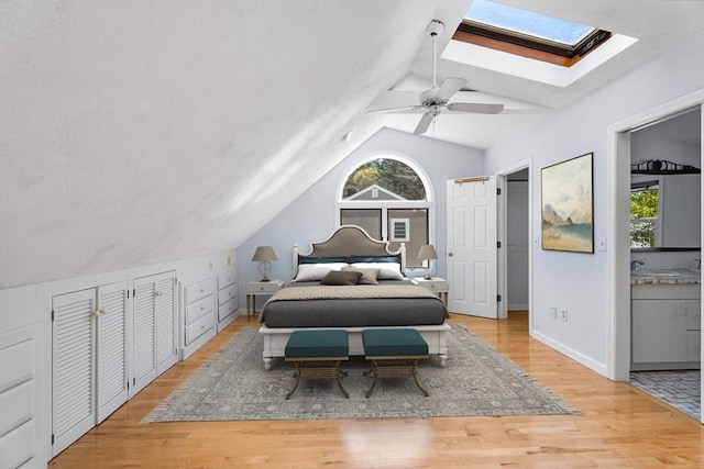 bedroom featuring a sink, vaulted ceiling with skylight, a ceiling fan, baseboards, and wood finished floors