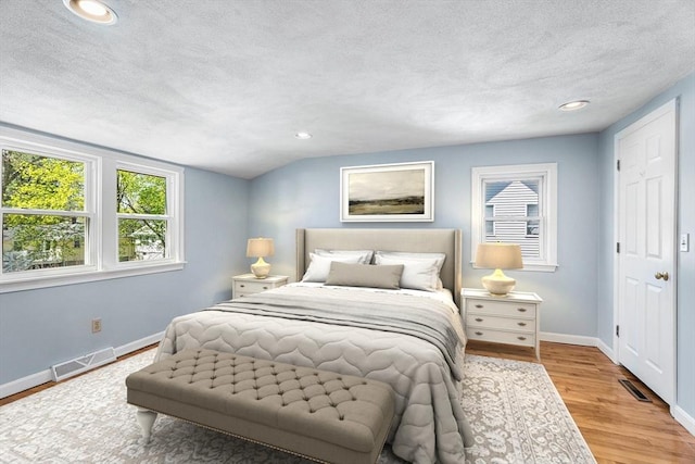 bedroom featuring visible vents, a textured ceiling, baseboards, and wood finished floors