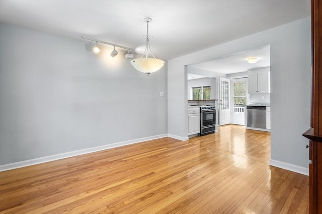 unfurnished dining area with baseboards, light wood finished floors, and track lighting