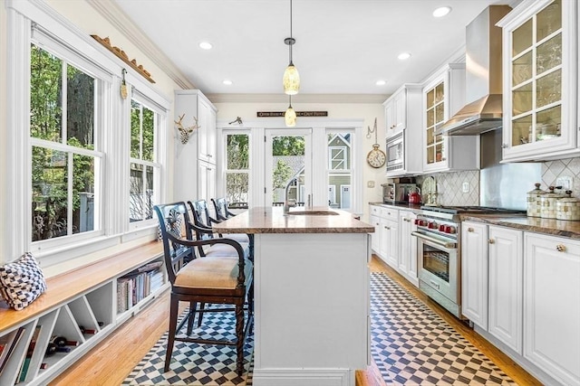 kitchen featuring pendant lighting, appliances with stainless steel finishes, white cabinets, wall chimney exhaust hood, and sink