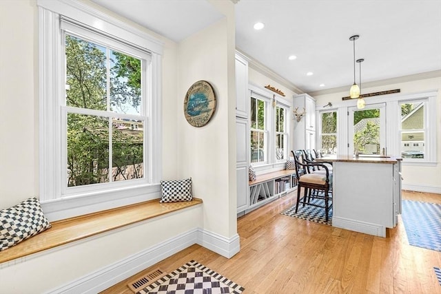 kitchen with white cabinets, light hardwood / wood-style floors, hanging light fixtures, a breakfast bar, and crown molding