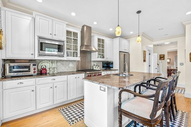 kitchen with appliances with stainless steel finishes, wall chimney exhaust hood, sink, light stone counters, and a kitchen island with sink