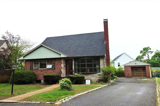 view of front of house with a chimney, brick siding, aphalt driveway, and a detached garage