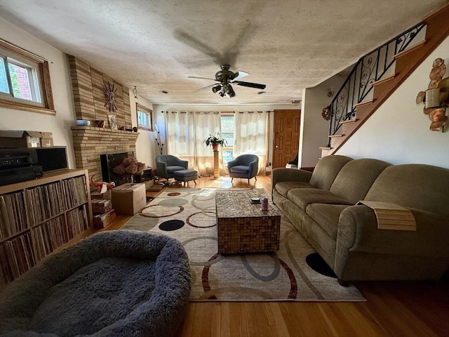 living area with ceiling fan, stairway, wood finished floors, and a brick fireplace