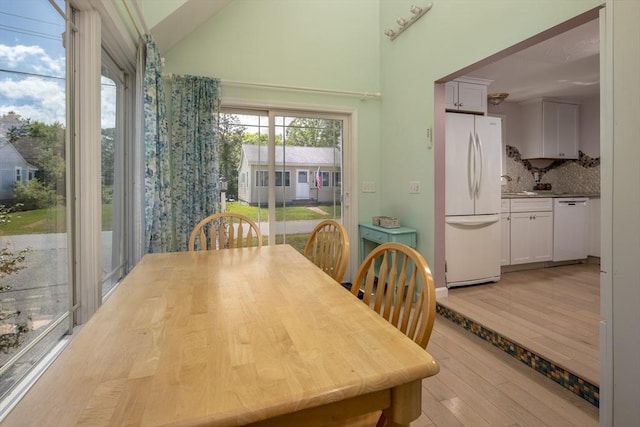 dining room featuring vaulted ceiling, sink, and light hardwood / wood-style flooring