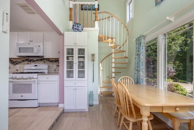 kitchen featuring white cabinetry, light wood-type flooring, backsplash, and white appliances