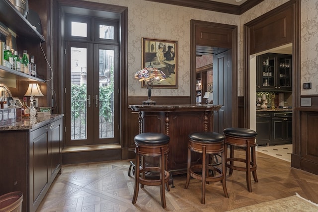 bar with light parquet floors, dark brown cabinetry, french doors, and dark stone countertops