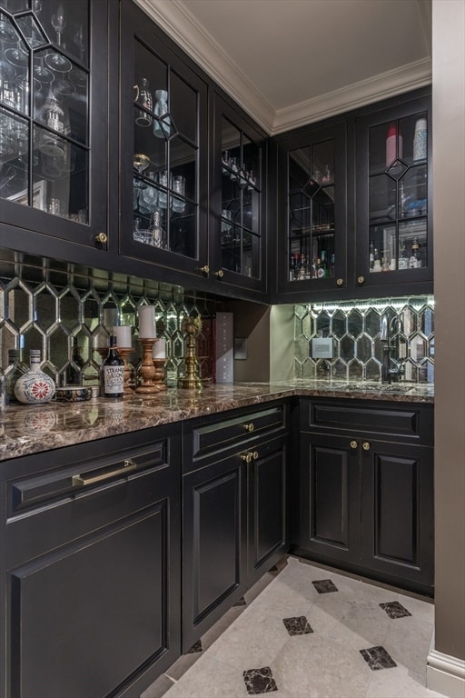 bar with dark stone countertops, tasteful backsplash, light tile floors, and ornamental molding