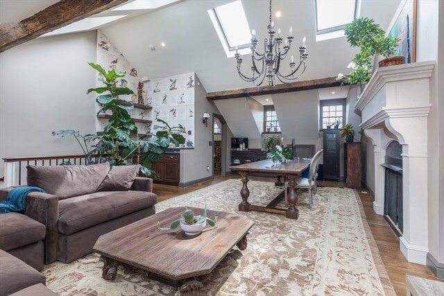 living room featuring a chandelier, a skylight, high vaulted ceiling, and light wood-type flooring