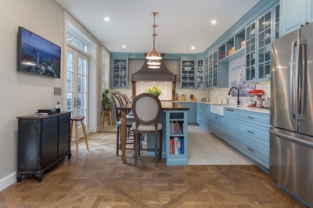 kitchen featuring dark parquet floors, custom range hood, blue cabinets, pendant lighting, and stainless steel fridge