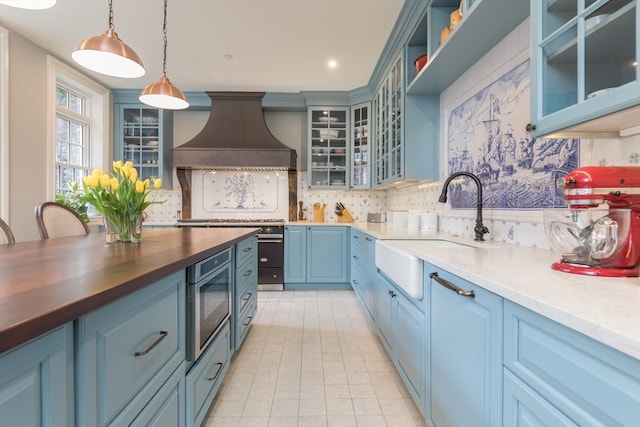 kitchen with sink, exhaust hood, hanging light fixtures, backsplash, and light tile flooring