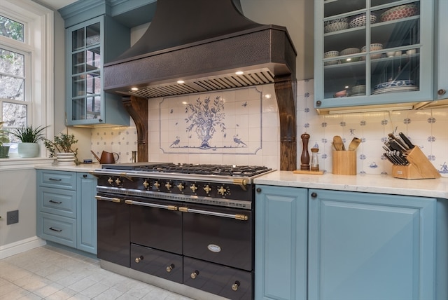 kitchen with light tile floors, double oven range, blue cabinets, backsplash, and custom range hood