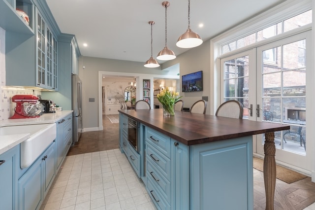 kitchen featuring decorative light fixtures, stainless steel refrigerator, french doors, butcher block countertops, and blue cabinetry