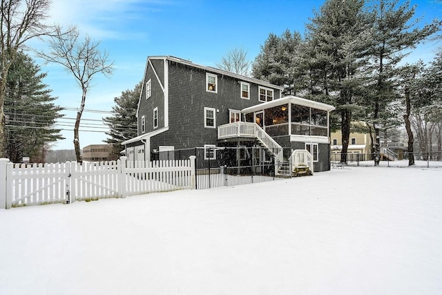 snow covered rear of property featuring a sunroom